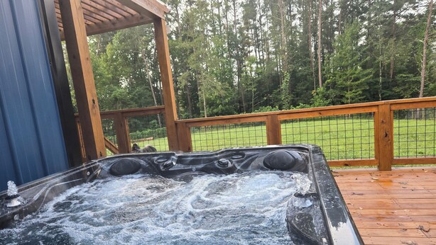 A hot tub on a wooden deck with a wooden pergola overhead.