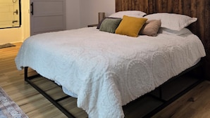 A bedroom with a bed, a ceiling fan, a wooden headboard, a painting, and a door leading to a bathroom.