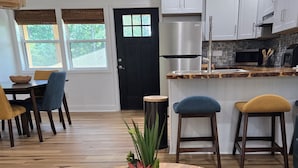 A modern kitchen with white cabinets, a round wooden table with a plant centerpiece, and a dining area with chairs and a rug.