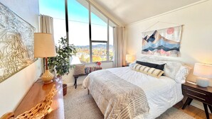 Ein modernes Schlafzimmer mit einem großen Bett, Blick auf die Stadt und einer Wanddekoration.