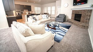 En moderne stue med en beige sofa, en grå lænestol og et sofabord. Der er en pejs med et tv ophængt over den.