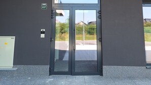 A modern building entrance with a glass door, a security camera, and a fire alarm button. - Sunset Dream Apartment (Sarajevo)