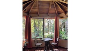 A room with a wooden ceiling, a table with two chairs, and a large window with curtains.