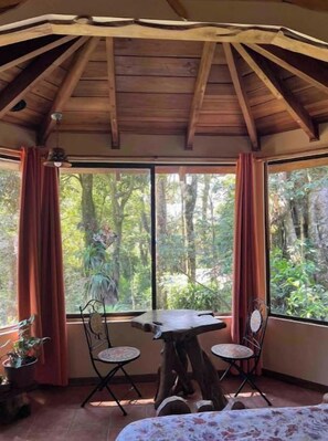 Una habitación con techo de madera, una mesa con dos sillas y un ventanal con cortinas.