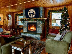 Un intérieur de chalet chaleureux avec une cheminée en pierre, des murs en bois, un sapin de Noël et des sièges confortables.