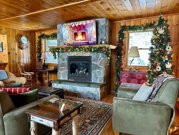 Un salon chaleureux avec une cheminée en pierre, des murs en bois, une horloge et des décorations festives.