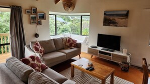 Una sala de estar con sofá, mesa de centro y televisor. Se ven ventanas con vistas a zonas verdes.
