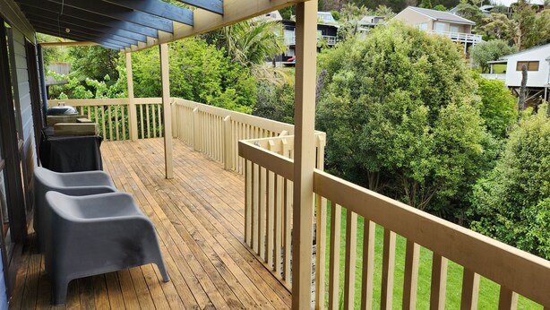 Terraza de madera con pérgola, mobiliario exterior y vistas a un jardín exuberante y casas.