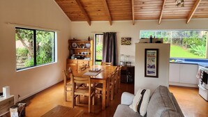 Amplia sala de estar con techo de madera, comedor con muebles de madera y vista a un jardín a través de grandes ventanales.