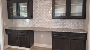 A kitchen with dark cabinets, a granite countertop, and a patterned backsplash.