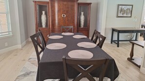 A dining area with a rectangular table set for six, surrounded by wooden chairs.