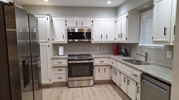 A modern kitchen with white cabinets, stainless steel appliances, and a granite countertop.