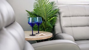 Un coin salon avec une table ronde en bois, deux verres bleus, une décoration en forme d’étoile de mer et une grande plante verte en arrière-plan.