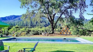 Zona de piscina con mesa y sillas, rodeada de abundante vegetación y montañas al fondo.