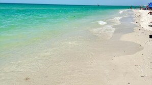 A beach with clear turquoise water, a sandy shore, and a few people in the distance. - New! Sunset Walk – Brand New Luxury Home, Just a Short Stroll to Vanderbilt Beach (Naples)