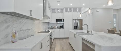 Una cocina moderna con armarios blancos, encimera de mármol y electrodomésticos de acero inoxidable.