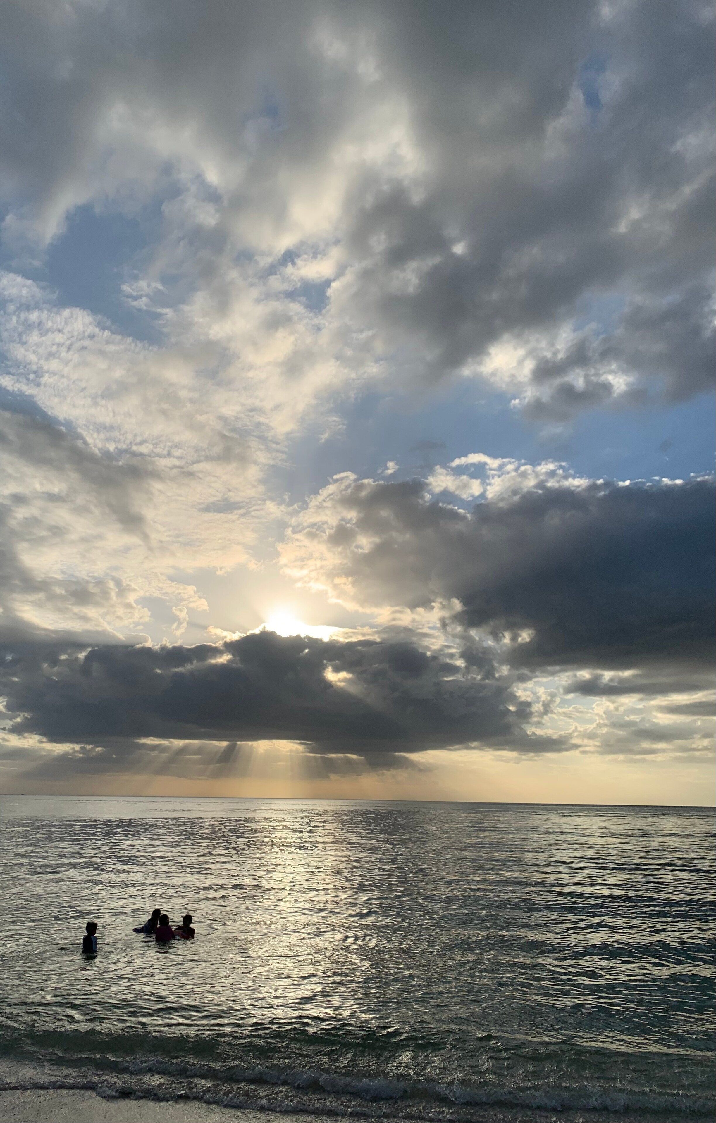 Une scène de plage avec des personnes dans l’eau et un coucher de soleil en arrière-plan.