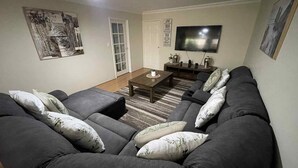 Ein Wohnzimmer mit einem dunkelgrauen Ecksofa, einem Couchtisch und einem flachbildfernseher, der an der Wand montiert ist.