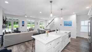 A modern kitchen with a large island, white cabinetry, and a view of the outdoors through large windows. - NEW Lakeside Cottage Sleeps 16 Includes Golf Cart Walk to Lake and Near Pool (Lakeside)