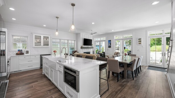 A modern kitchen with white cabinetry, a central island, and a dining area with a large table and chairs. - NEW Lakeside Cottage Sleeps 16 Includes Golf Cart Walk to Lake and Near Pool (Lakeside)
