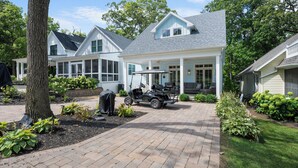 A house with a covered patio, a golf cart, and a well-maintained garden. - NEW Lakeside Cottage Sleeps 16 Includes Golf Cart Walk to Lake and Near Pool (Lakeside)