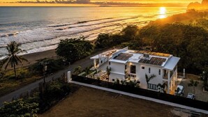 A coastal property with a white building, solar panels, and a view of the ocean at sunset. - Luxury Beachfront Villa! Newest Home in Jaco! (Jaco)