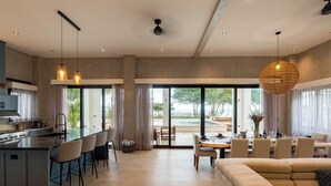 A modern kitchen with a central island, bar seating, and a dining area with a large window. - Luxury Beachfront Villa! Newest Home in Jaco! (Jaco)