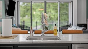 Una cocina moderna con un lavamanos de acero inoxidable, una botella de detergente Meyer’s y una tableta sobre una encimera.