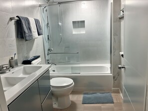 Ett modernt badrum med en dusch som är avskärmad med glasväggar, ett vitt badkar och en toalett.