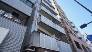Un edificio de varios pisos con un diseño arquitectónico moderno, que presenta balcones con celosías de metal y elementos estructurales visibles, como tuberías y vigas.