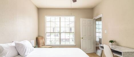 Ein Schlafzimmer mit einem Bett, einem Schreibtisch, einem Stuhl, einem Deckenventilator und einem Fenster mit Jalousien.
