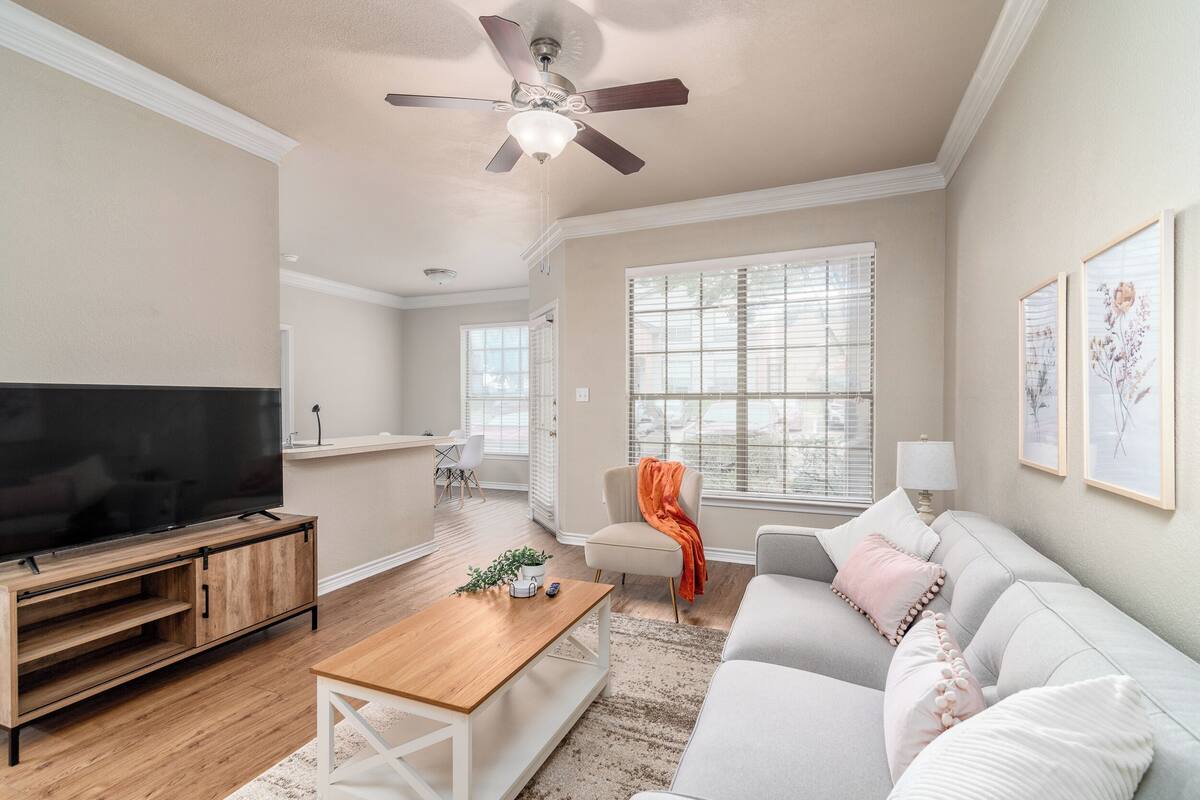 A living room with a flat-screen TV, wooden entertainment unit, white sofa, and a ceiling fan.