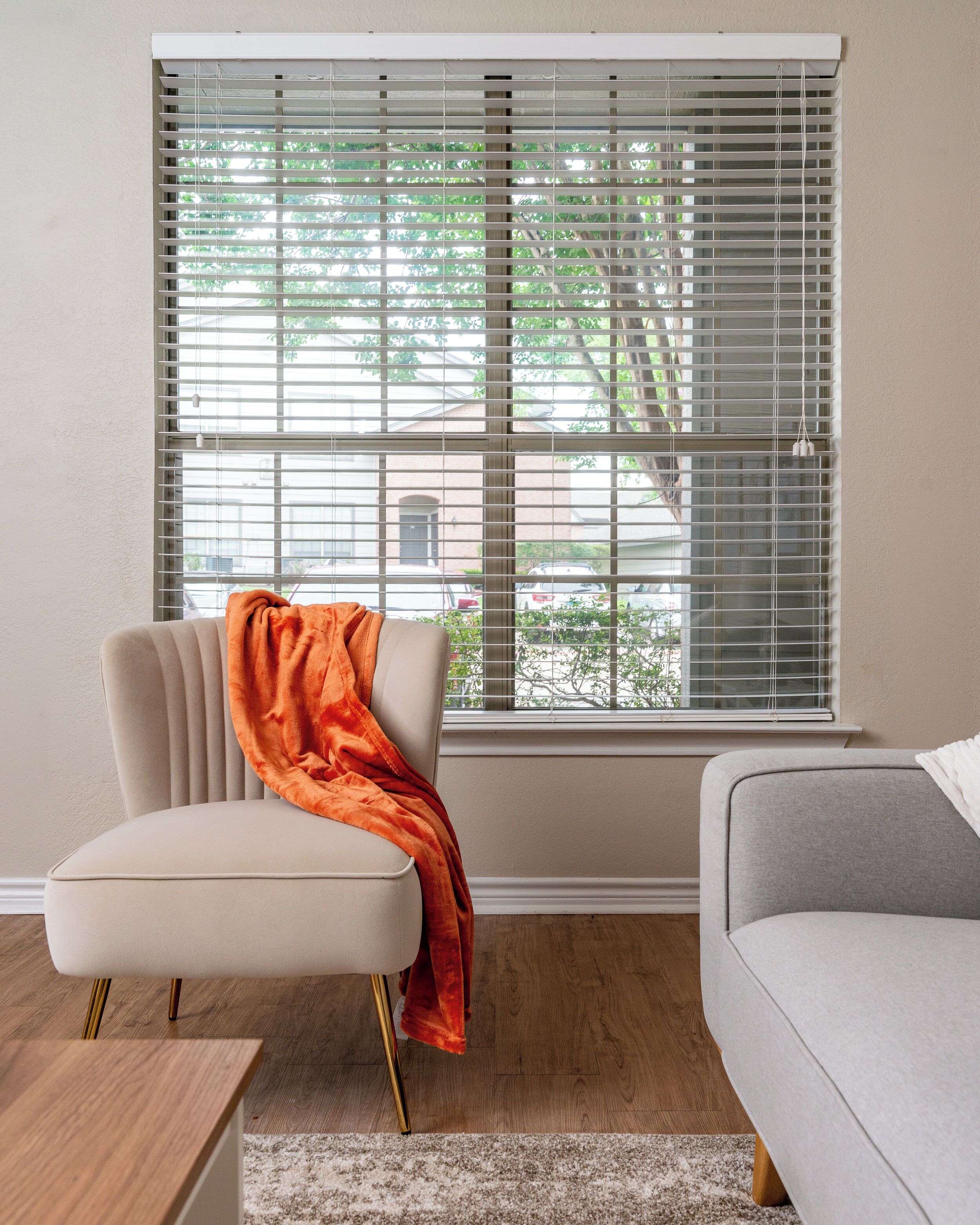 A room with a window, a beige armchair, a grey sofa, and a wooden coffee table.