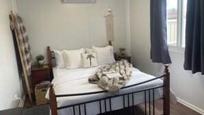 A bedroom with a bed, bedside tables, a wall-mounted air conditioner, a window with curtains, and a wooden floor. - Wannanup Retreat Short Stay Accommodation. Pet-Friendly! (Wannanup)