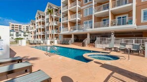 A hotel with a swimming pool, outdoor seating, and a multi-story building with balconies.