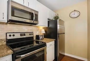 A compact kitchen with a microwave, stove, oven, refrigerator, and a clock on the wall. - Festival Sale! Amazing Balcony View~Pool & Hot Tub (Gulf Shores)