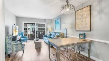 A modern living room with a dining table, blue patterned sofa, and a chandelier.