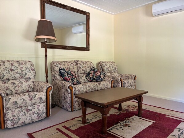 A living room with two floral-patterned armchairs, a wooden coffee table, and a large mirror on the wall. - School cottage (Walhalla)