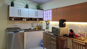 A compact kitchen with a washing machine, a coffee maker, and a small dining area with a chair. - Vilars154- Knights and Lagoon (Macaé)