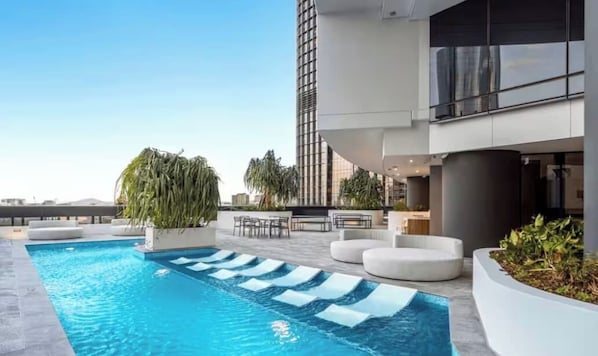 Un espace piscine sur le toit, doté d’une piscine moderne, de coins salon et offrant une vue sur un grand immeuble.
