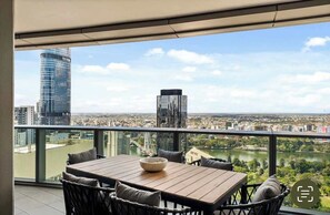 Un balcon avec une table et des chaises, offrant une vue sur la ville, avec ses bâtiments et sa rivière.