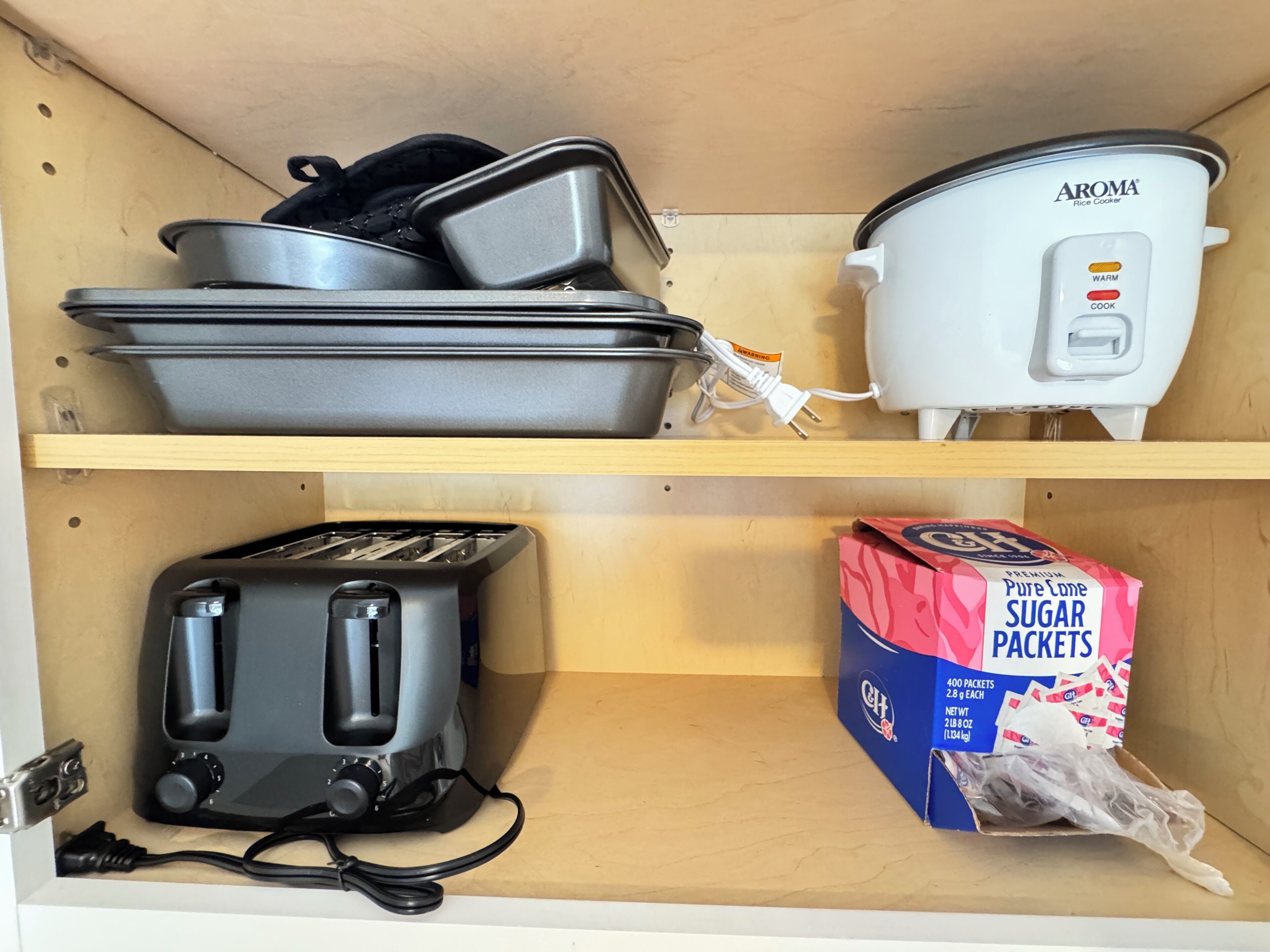 A kitchen with a toaster, a rice cooker, and a box of sugar packets.