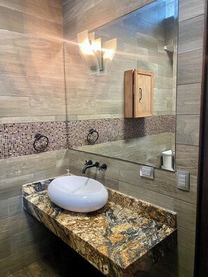 Ein modernes Badezimmer mit einer Granit-Arbeitsplatte, einem weißen Waschbecken und einem Spiegel darüber.