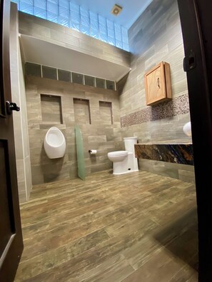 Ein modernes Badezimmer mit Oberlicht, Toilette, Urinal und Holzschrank.