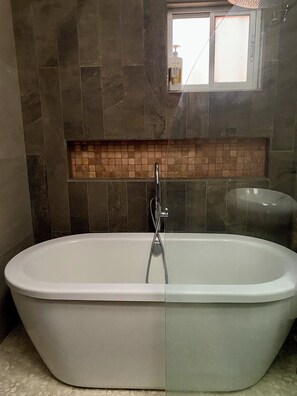 Ein modernes Badezimmer mit einer freistehenden Badewanne, einem gefliesten Duschbereich und einem Fenster über der Dusche.