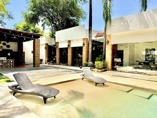 A pool area with lounge chairs, a barbecue setup, and a glass-enclosed restaurant.