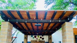 An outdoor patio with a wooden table and benches, a brick wall, and a ceiling with exposed beams.
