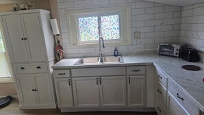 A kitchen with white cabinets, a double sink, a window with stained glass, and a toaster on the counter. - Quaint Country Home with Hot Tub (Crown Point)