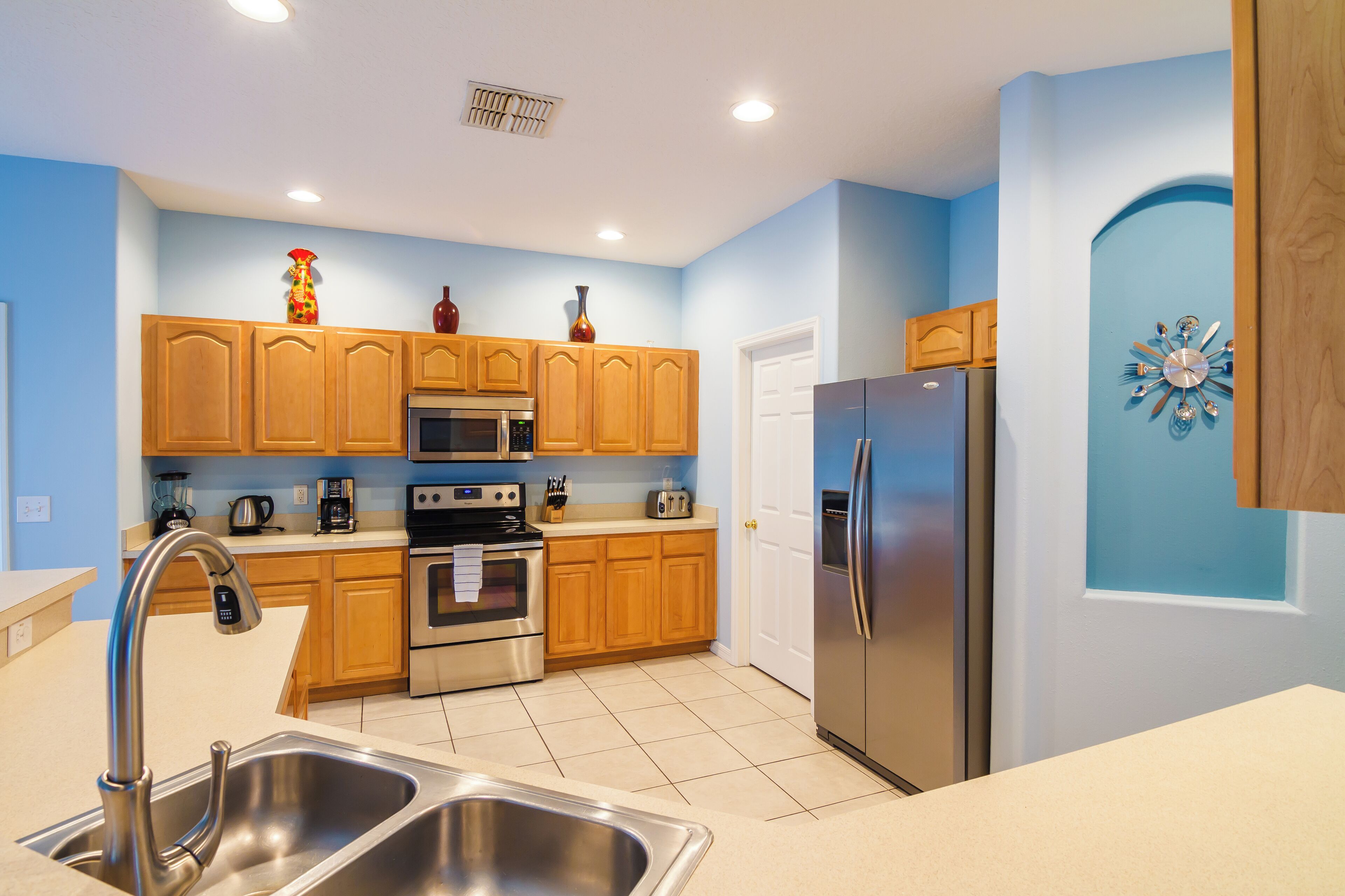 A modern kitchen with wooden cabinets, stainless steel appliances, and a blue accent wall.