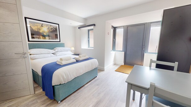 Una habitación de hotel moderna con una cama bien hecha, una mesa de comedor y un ventanal grande.